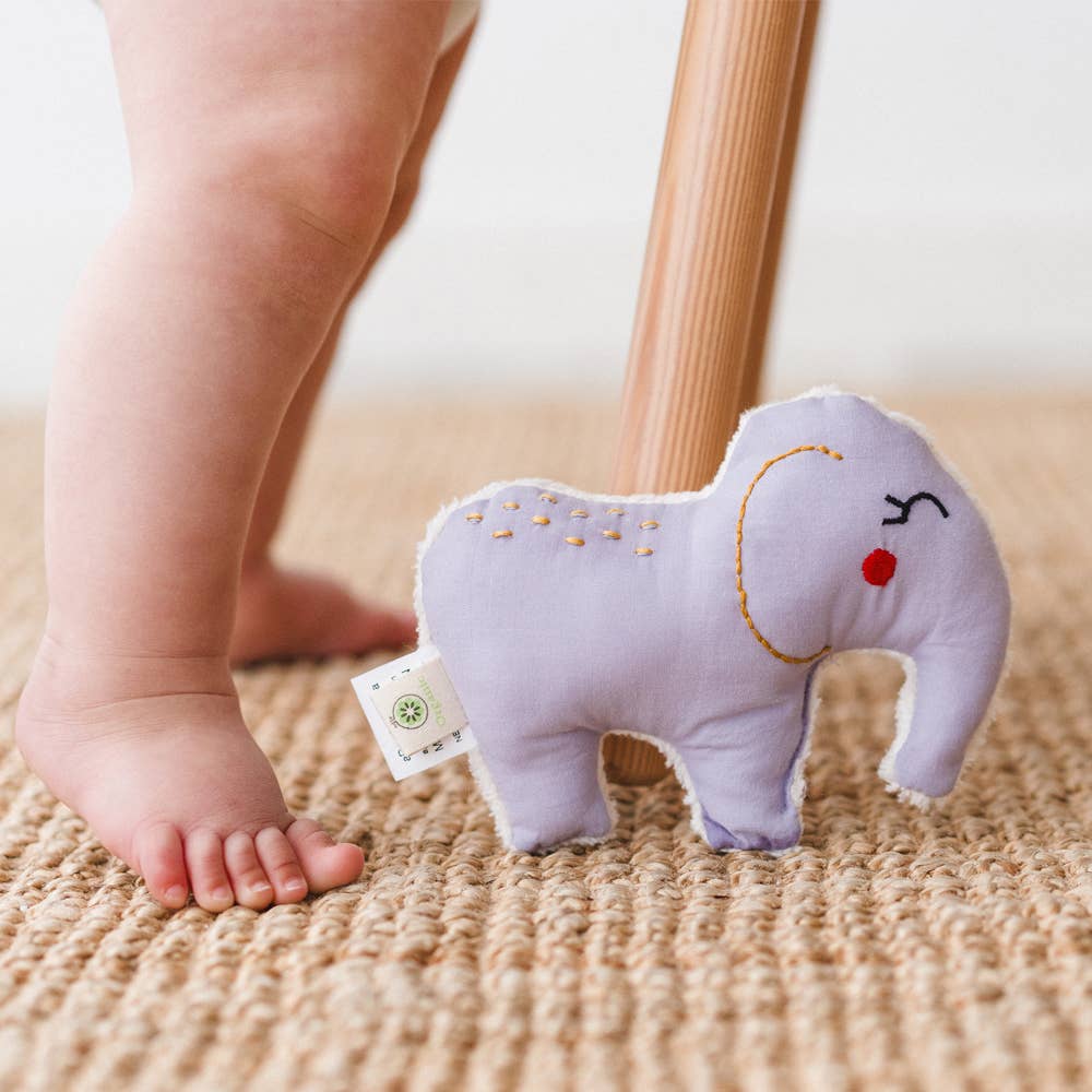 Baby standing with organic cotton elephant rattle