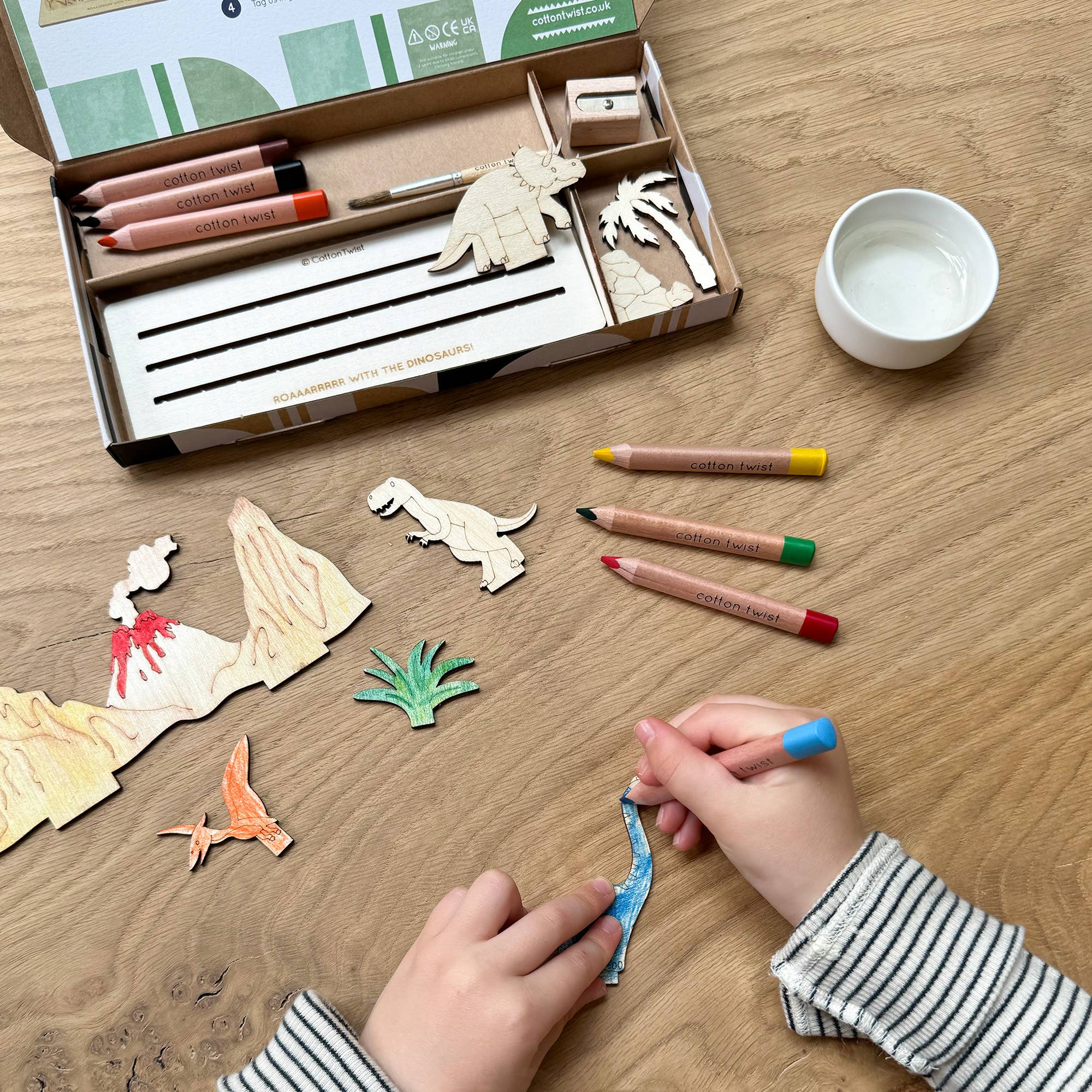 Child painting wooden dinosaur with watercolour pencils